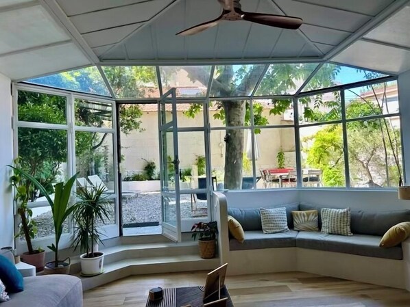 A sunlit room with a curved bench, large windows, and a ceiling fan. - By the sea, a magnificent 150-square-meter apartment with a garden (Marseille)