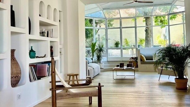 A spacious living room with a wooden floor, white walls, and a large window providing a view of greenery outside. - Seaside, magnificent 150m2 apartment with garden (Marseille)