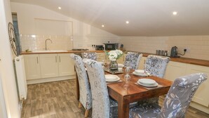 A modern kitchen with white cabinets, a wooden dining table, and patterned chairs. - The Apartment at Plas Yr Eithin (Amlwch)