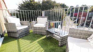 A patio with wicker furniture and a glass table, surrounded by a metal fence. - The Apartment at Plas Yr Eithin (Amlwch)