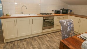 A modern kitchen with white cabinets, a stainless steel sink, a gas stove, and a microwave. - The Apartment at Plas Yr Eithin (Amlwch)