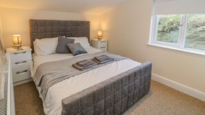 A bedroom with a large bed, two bedside tables, a window, and a view of greenery outside. - The Apartment at Plas Yr Eithin (Amlwch)