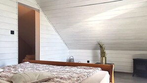 Ein Schlafzimmer mit schrägen Wänden, einem Bett mit floralem Überwurf, einem kleinen Tisch mit einer Vase und einem dunklen Nachttisch.