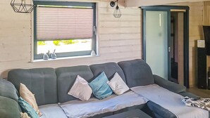 Ein Wohnzimmer mit einer Couch, einem Fenster mit Jalousien, einer Tür und einer Wandleuchte.