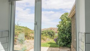 A view from a window with a sliding door, overlooking a garden with a variety of plants and a hill in the distance. - The Headland (Amlwch)
