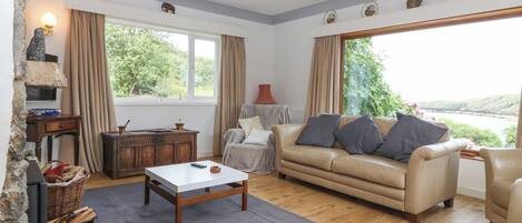 A living room with a sofa, a coffee table, a fireplace, a television, and a view of the outdoors.