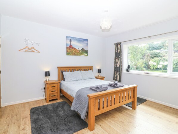 A bedroom with a wooden bed, bedside tables, a nightstand, a window with a view of greenery, and a painting on the wall.