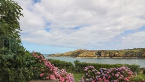 A coastal landscape with a rocky hill, a lighthouse, and a body of water. - The Headland (Amlwch)