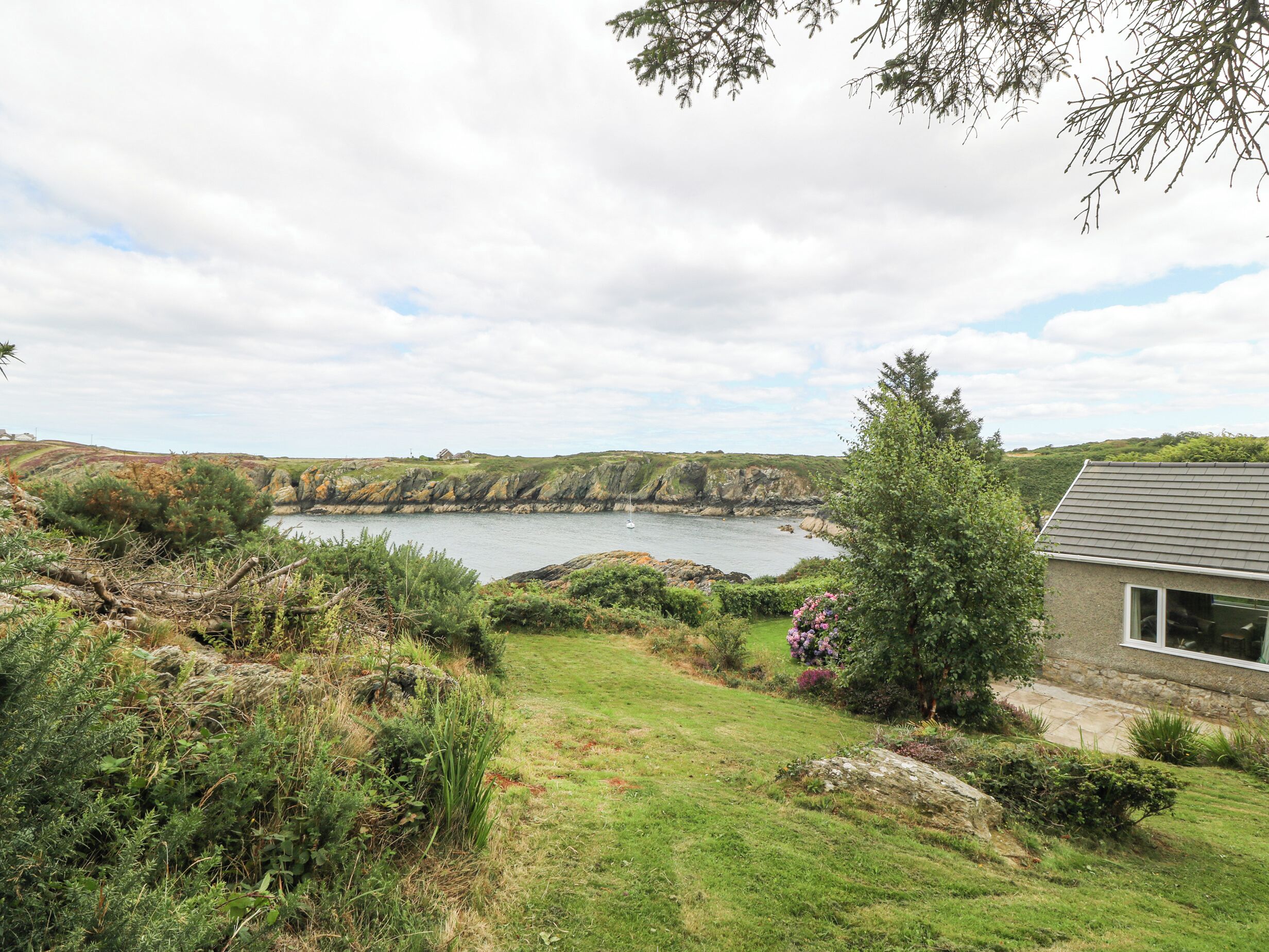 A coastal landscape with a grassy area, a stone building, and a view of the sea and cliffs.