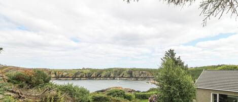 A coastal landscape with a grassy area, a stone building, and a view of the sea and cliffs.