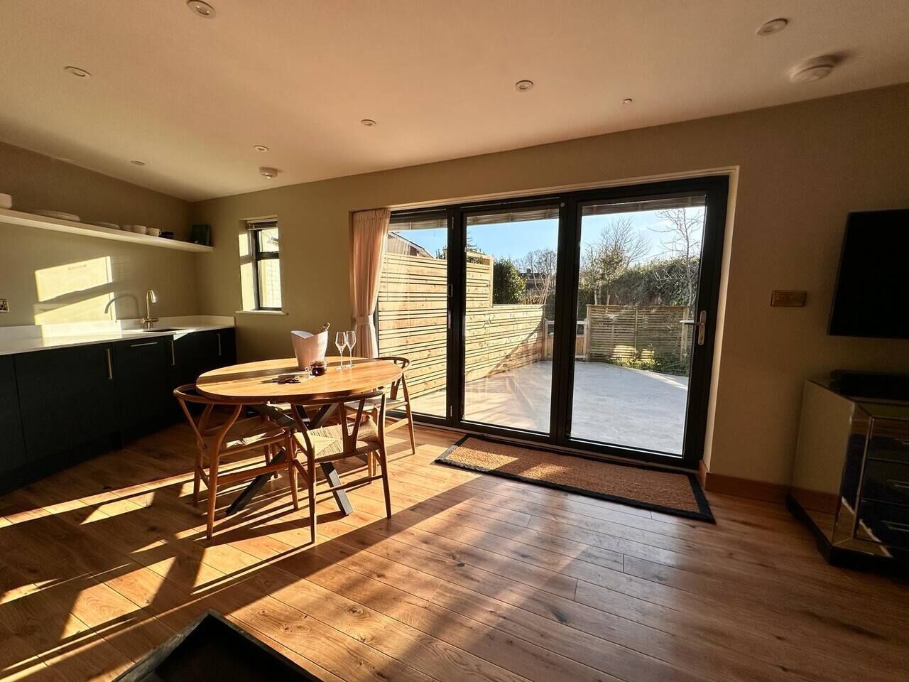 A spacious kitchen with a dining area, large sliding glass doors leading to a backyard, and a flat-screen TV.