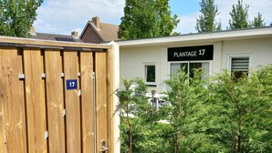 Ein hölzernes Tor mit der Nummer 17, ein Gebäude mit der Aufschrift 'PLANTAGE 17' und umgebende Grünflächen.