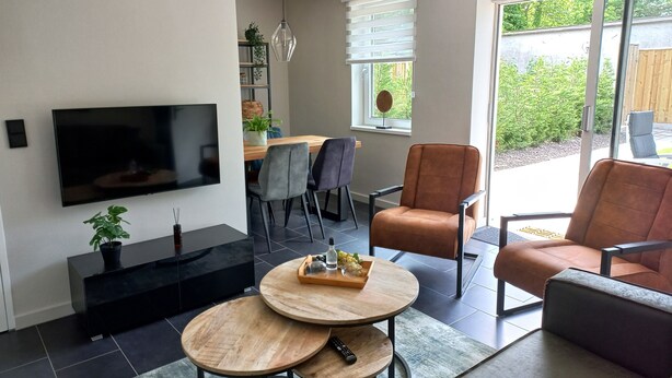Ein modernes Wohnzimmer mit einem Flachbildfernseher, zwei runden Holztischen, einem Sofa und einem Sessel.