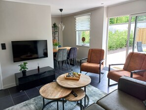 A modern living room with a flat-screen TV, two round wooden tables, a sofa, and a chair. - Charming vacation home with a garden and terraces in the center of the village (Bruinisse)