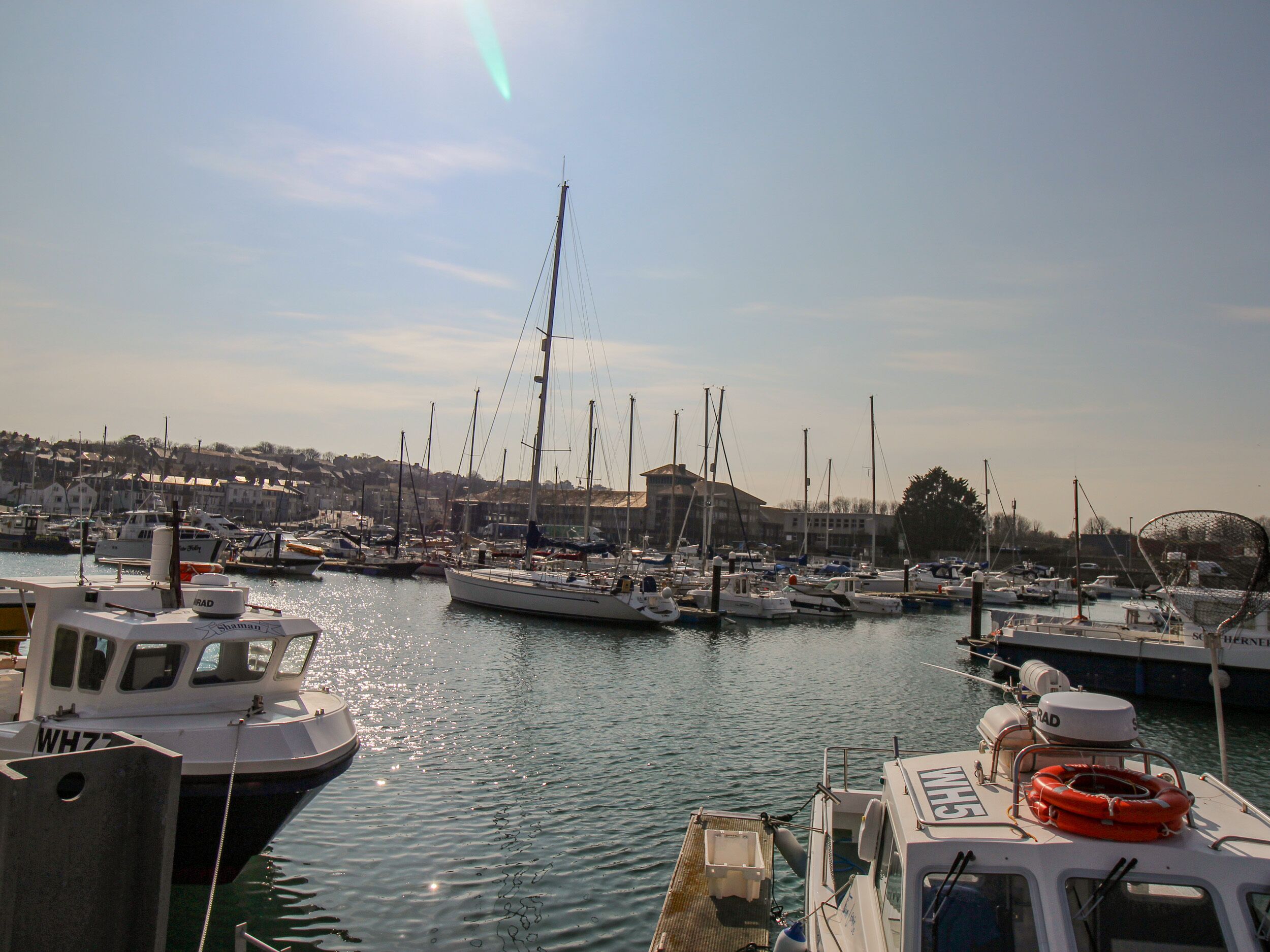 A marina with various boats docked, a clear sky, and a distant town.