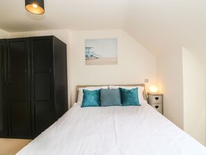 A bedroom with a bed, a nightstand, a wall-mounted shelf, and a wardrobe. - Harbour Reach 6 (Weymouth)
