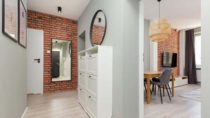 A modern apartment with a brick accent wall, a white wardrobe, a dining area with a table and chairs, and a hanging light fixture.
