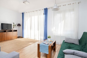 Un salon moderne avec un téléviseur à écran plat, des meubles en bois, un canapé vert et des rideaux en voile.