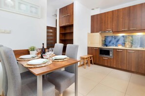A modern kitchen with wooden cabinets, a dining table set for two, and a small stool.