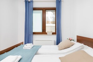 A bedroom with a bed, a window with curtains, a radiator, and a small table with a flower vase.