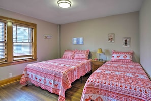 Een slaapkamer met twee bedden, houten vloeren, een raam met zonwering en decoratieve wandversieringen.