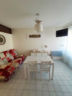 A dining area with a white table and chairs, a ceiling fan, a wall-mounted TV, and a patterned sofa.