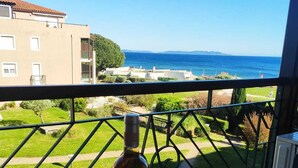 Un balcone con un tavolo apparecchiato per due persone, una bottiglia e dei bicchieri, con vista sulla costa, edifici e vegetazione.