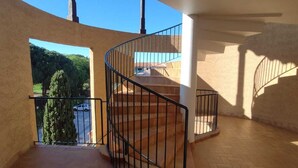 Un ambiente spazioso con una scala a forma di ferro di cavallo, un balcone affacciato sul verde e sull'acqua, e un pavimento piastrellato.