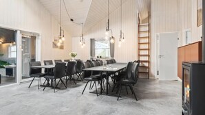 Un espace de salle à manger moderne avec une longue table, des chaises noires et des luminaires suspendus.