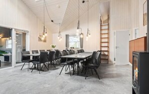 Cozy dining area with a long table and black leather chairs, featuring a high ceiling with exposed beams and pendant lights.