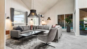 Un salon moderne avec un canapé d’angle, une table basse et des luminaires suspendus.