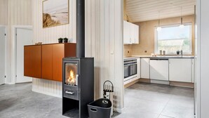 Une cuisine moderne dotée d’un poêle à bois, de meubles blancs et d’une fenêtre donnant sur un jardin.