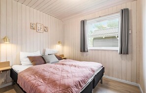 Relax in this serene bedroom with a plush bed, adorned with a vibrant quilt and multiple pillows, and enjoy the natural light pouring in through the large window.