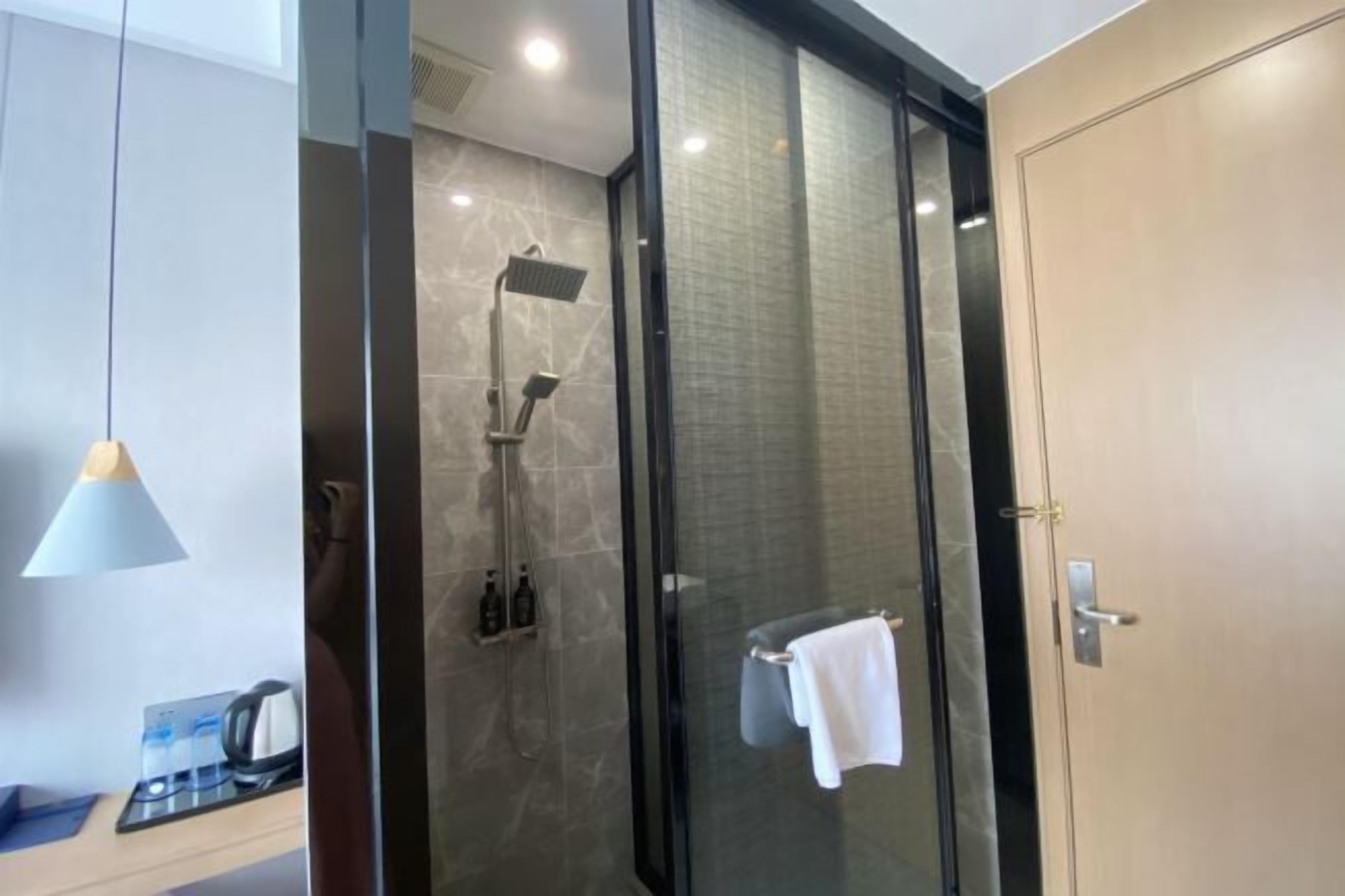 A modern bathroom with a glass-enclosed shower, a towel rack, and a coffee machine on the counter.