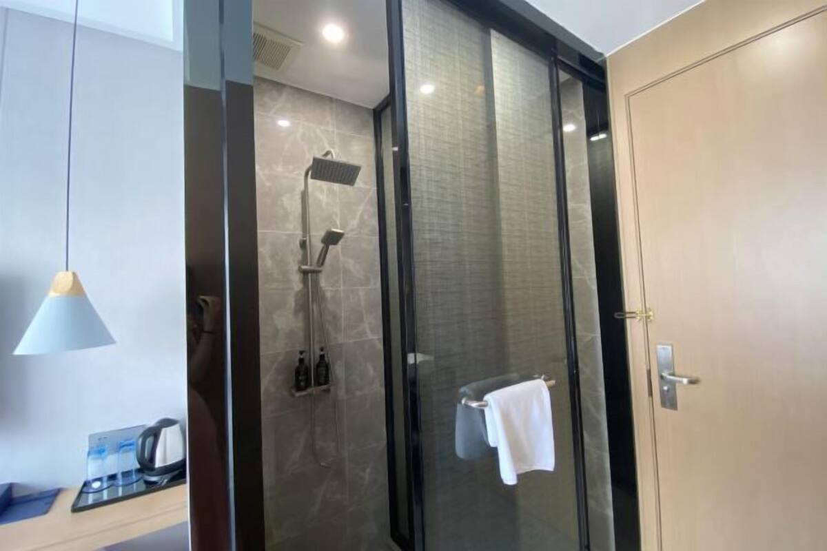 A modern bathroom with a glass-enclosed shower, a towel rack, and a coffee machine on the counter.