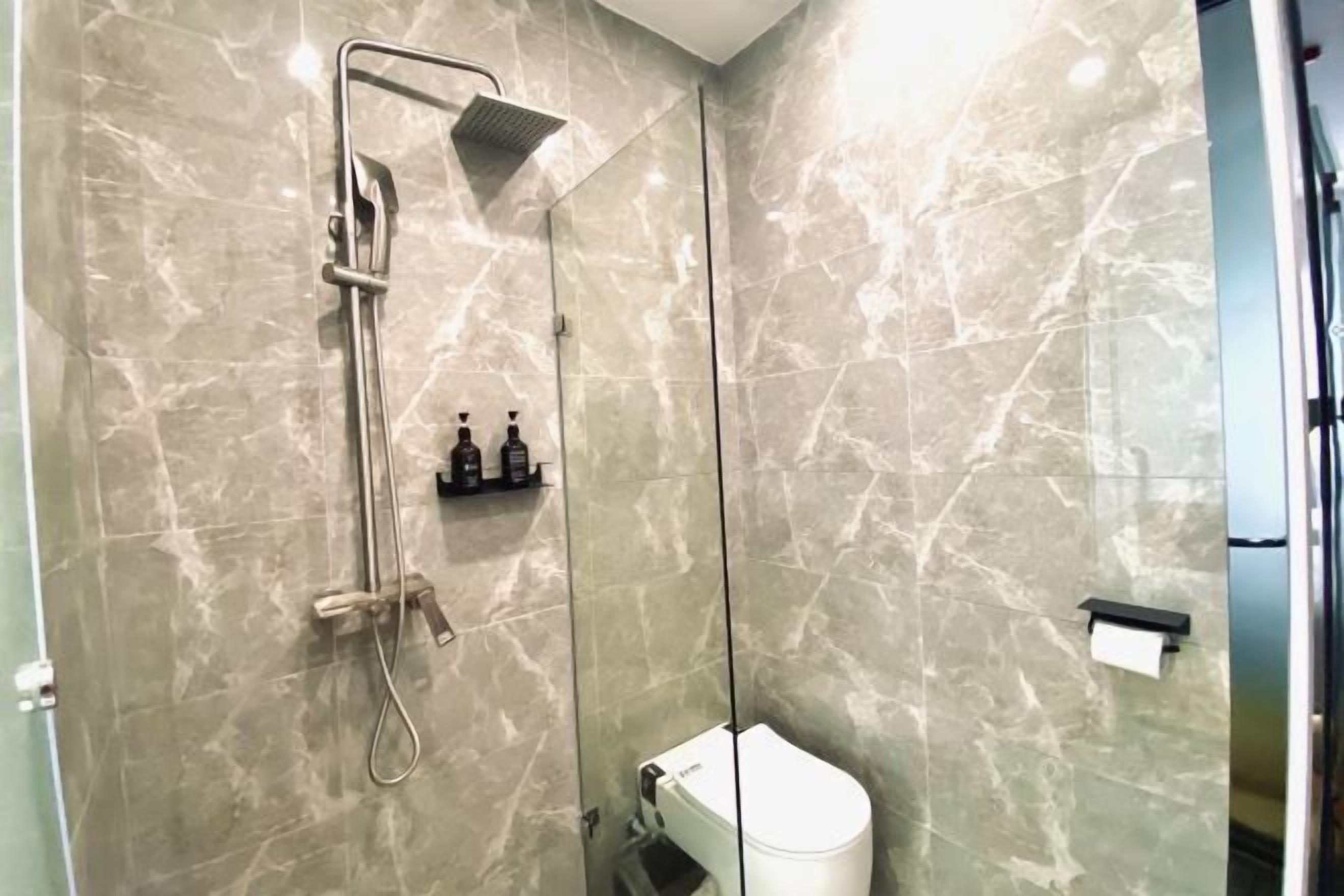 A modern bathroom with a glass-enclosed shower, a toilet, and a marble wall.