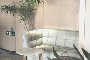 A corner seating area with a cushioned sofa and a small round table, a potted plant, and an exit sign on the wall. - Shenzhen Aige Hotel (Clothing Wholesale Market Nanyou Metro Station Store) (Shenzhen)