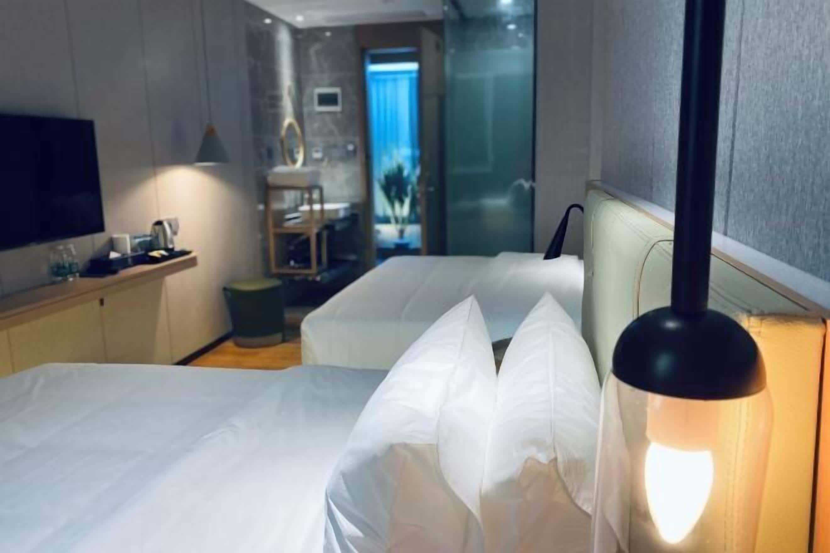A hotel room with two beds, a TV, a desk with a lamp, and a view of a hallway.