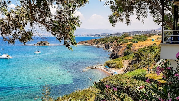 A coastal view with clear blue waters, boats, and a beach area with umbrellas.