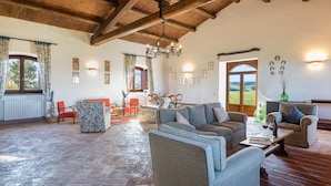 A spacious living room with a high ceiling, wicker furniture, and a view of the countryside through a large window.