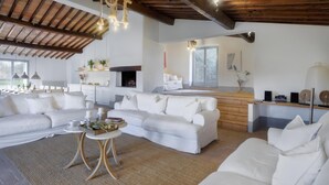 A spacious living room with a large sectional sofa, a coffee table, and a fireplace. There is a kitchen area with a wooden countertop and a dining table. - Villa Carmeli 12 2 in Acquapendente (Acquapendente)