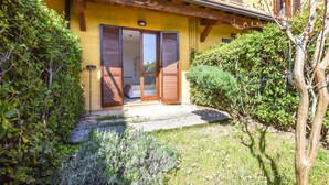 A yellow building with a wooden door and shutters, surrounded by greenery.
