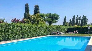 A swimming pool with lounge chairs and a neatly trimmed hedge.