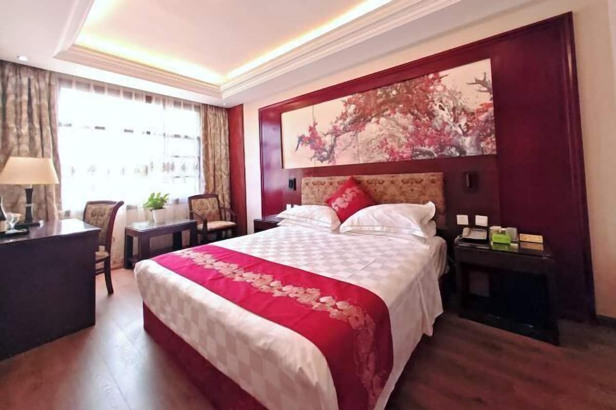 A hotel room with a large bed, a desk with a lamp, a chair, and a nightstand with a phone.
