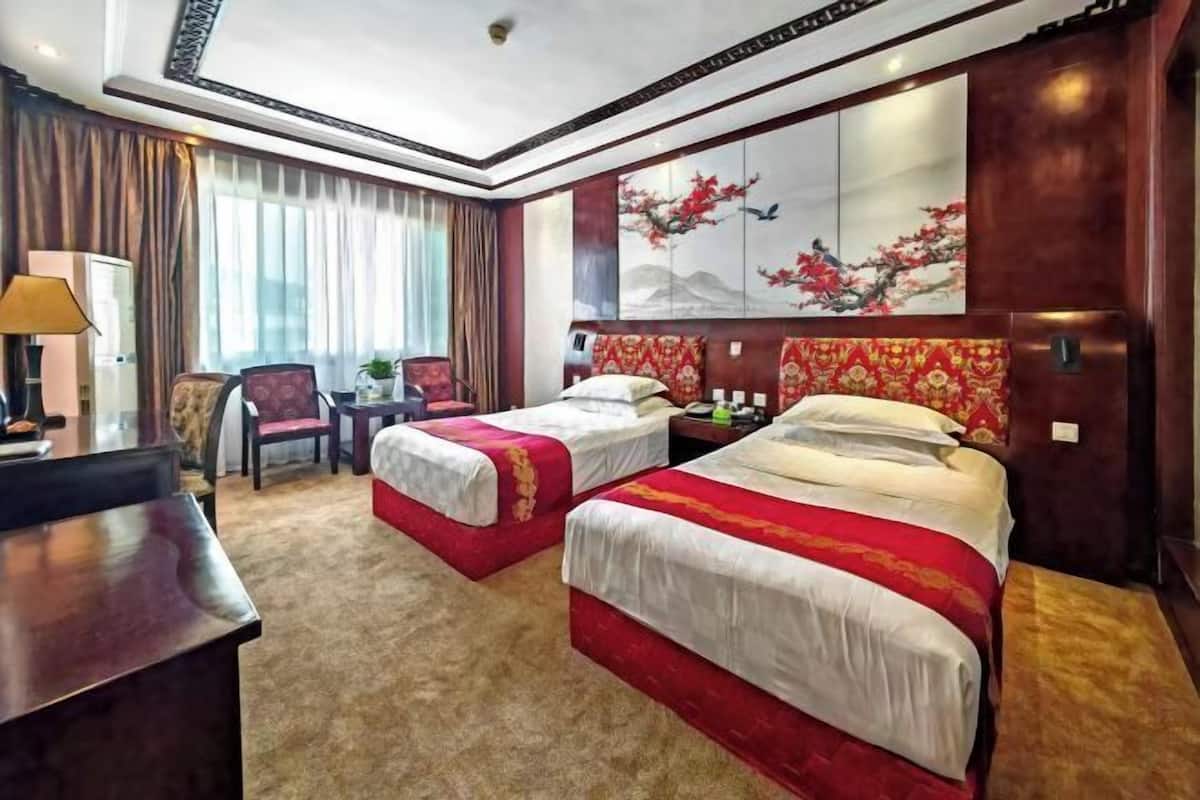 A hotel room with two beds, a desk, a chair, and a large window with curtains.