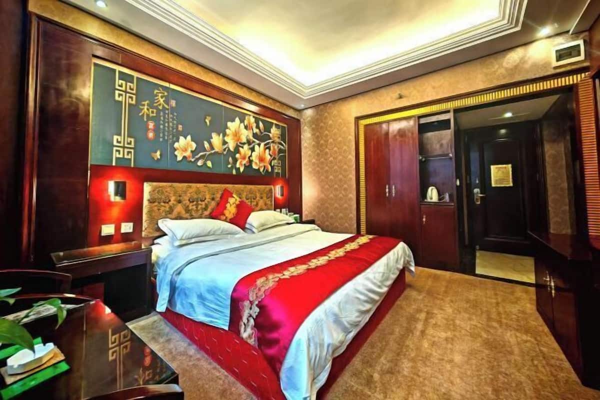 A hotel room with a large bed, a wooden headboard, a decorative wall with floral patterns, and a wardrobe.