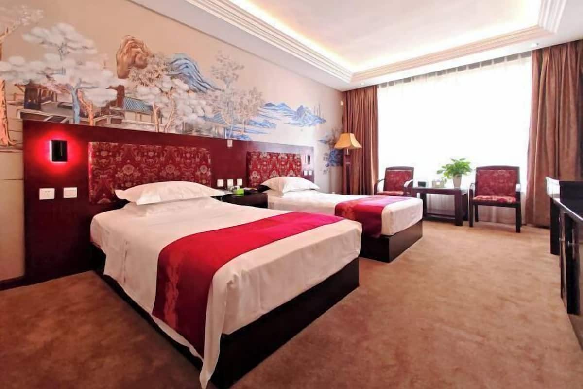 A hotel room with two beds, a large mural on the wall, a desk with a chair, and a large window with curtains.