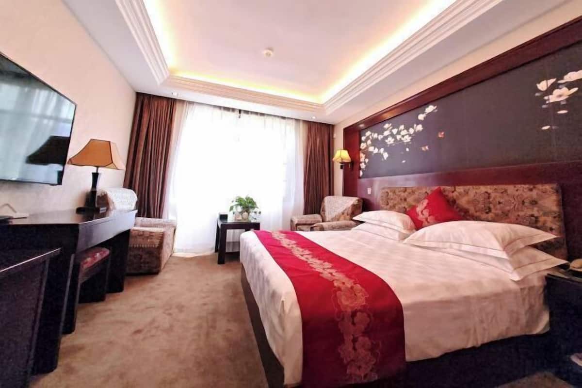 A hotel room with a large bed, a desk, a chair, a TV, and a window with curtains.