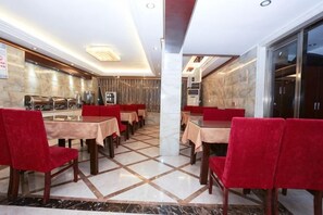 A restaurant with marble flooring, red upholstered chairs, and tables with beige tablecloths. - Ligang Hotel (Xishui)