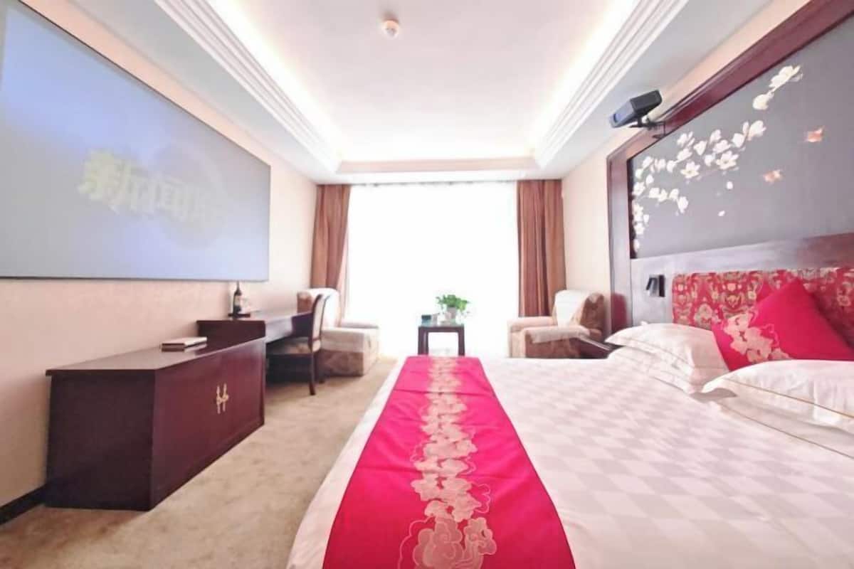 A hotel room with a bed, a desk, a chair, a TV screen, and a window.